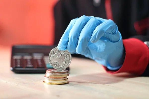 a silver australian coin held on a pile of coins by a person wearing blue gloves against a colored wall