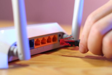 Masa ve pembe arka planda antenler ile internet kablosu yönlendiriciye bağlanıyor