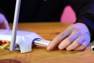 Siyah eşofmanlı bir insan tarafından ahşap bir masada iki anten bulunan beyaz bir yönlendiriciye gsm modemi yerleştiriliyor.