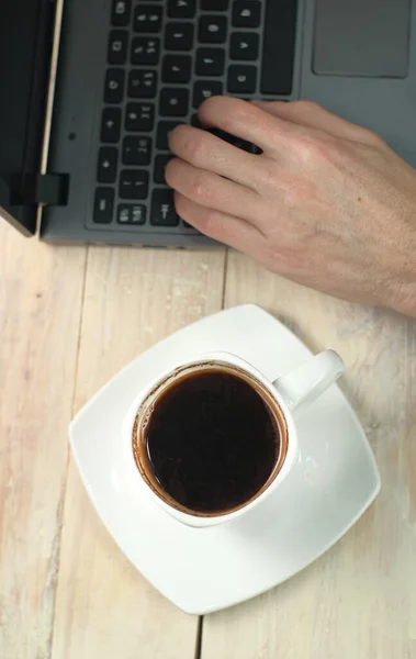 a cup of coffee on the table with a laptop and a hand from above