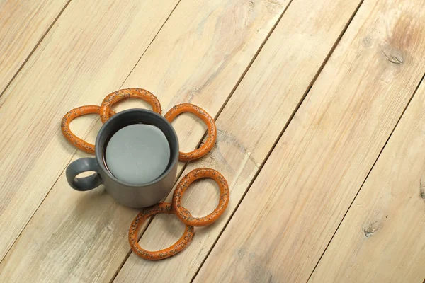 a mug with coffee next to a bagel on a plank table