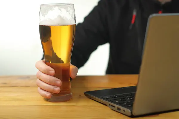 mug with beer in hand next to laptop on wooden table