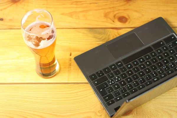 mug with beer next to laptop on wooden table