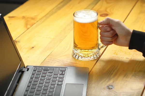 mug with beer in hand next to laptop on wooden table