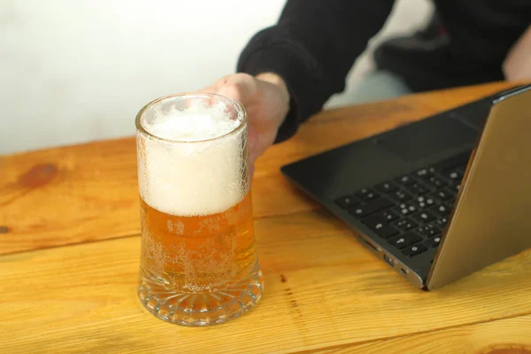 mug with beer in hand next to laptop on wooden table