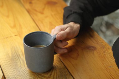 person holding a mug with coffee on a plank table