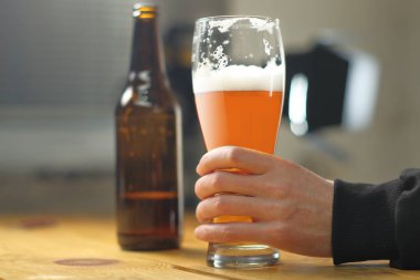 person holding a mug with beer on the table and a bottle in the background