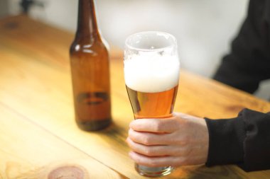 person holding a beer mug next to a bottle on a wooden table