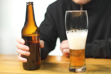 person holding a bottle with beer on the table next to the mug