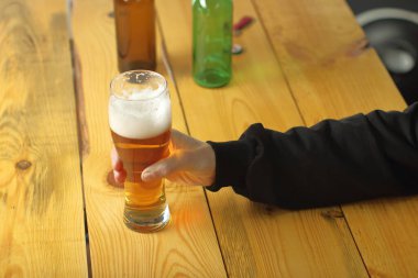person holding a full pint of beer on the table and background of bottles
