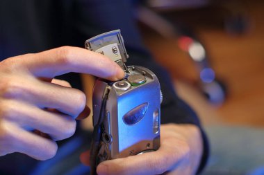 Arka planda bir kişi eski bir fotoğraf makinesinden hafıza kartı çıkarıyor.