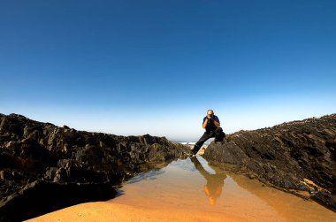 Okyanusun kıyısındaki kayaları fotoğraflayan adam.