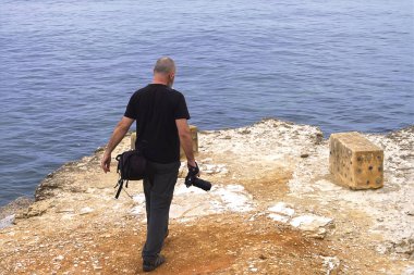 Okyanusun kenarında kamerası olan siyahlı bir adam.