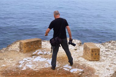 Okyanusun kenarında kamerası olan siyahlı bir adam.