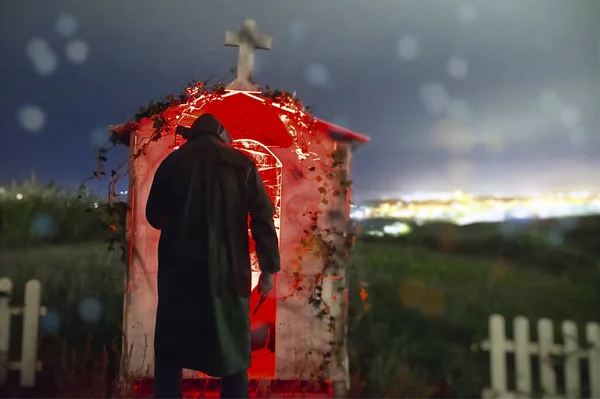 Blurred silhouette of man in halloween costume standing at grave in cemetery.