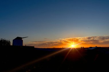 Yel değirmeninin siluetiyle kırsalda gün batımı.