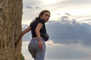 Gökyüzünün arka planında siyah tişörtlü ve kot pantolonlu güzel bir genç kız.