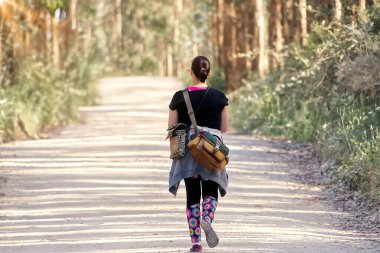 Sırt çantalı genç bir kadın ormanda toprak yolda yürüyor. Arka plan