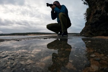 Fotoğrafçı, deniz çekildiğinde kumsalda bir kamerayla fotoğraf çekiyor.