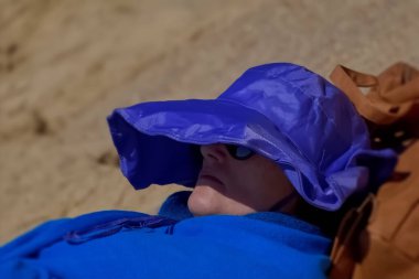 Mavi yağmurluklu ve plajda şapkalı bir kadın.