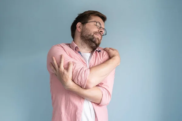 stock image Man embraces himself, dreamily closing eyes. Isolated, on a blue background.