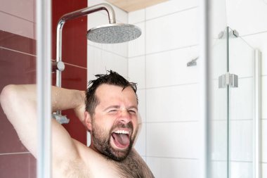 Duştaki adam pozitif, eğleniyor ve sıcak suyun altında durmaktan zevk alıyor. Yakın plan..