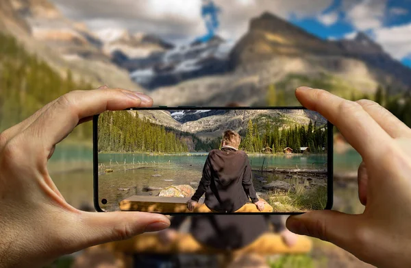 stock image Tourist taking a picture with a mobile phone of a man resting on a bench at the Lake O'Hara, Yoho National Park.