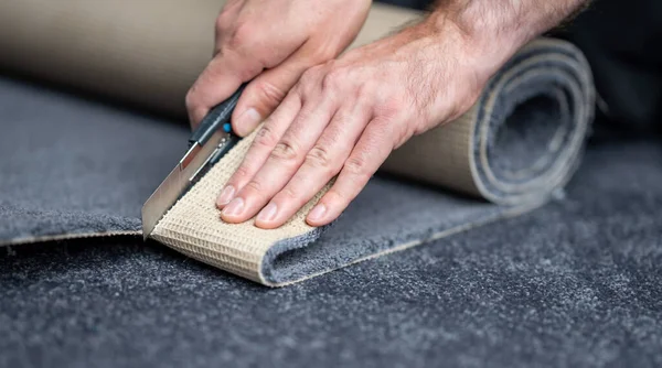 Handyman cutting a new carpet with a carpet cutter..	