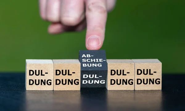 Symbol for deporting asylum seekers. Hand turns one black cube and changes the German word \'Duldung\' (acceptance) to \'Abschiebung\' (deportation).