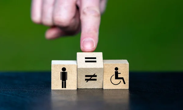 Symbol for equal rights of persons with disabilities. Hand turns wooden cube and changes the unequal sign to a equal sign.