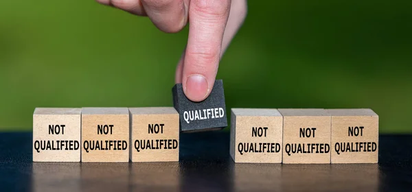 Symbol for finding a qualified candidate. Hand picks wooden cube with the text \'qualified\' instead of cubes with the text \'not qualified\'.