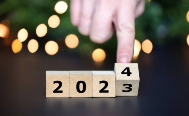 Hand turns cube and changes the year 2023 to year 2024.	