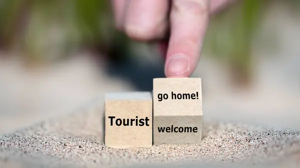 stock image Hand turns cube and changes the expression 'tourist welcome' to 'tourist go home!'.