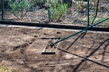 Adam bahçedeki zemini düzleştirmek için çim tırmığı kullanıyor. Eşitsizliği eşitlemek ve mükemmel bir çimenliğe zemin hazırlamak için..