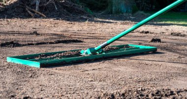 Adam bahçedeki zemini düzleştirmek için çim tırmığı kullanıyor. Eşitsizliği eşitlemek ve mükemmel bir çimenliğe zemin hazırlamak için..