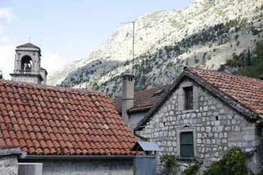Çan kulesi Kotor 'un tarihi taş binaları ve terasotta çatıları arasında dimdik duruyor. Eski tahkimatlar dağ yamacına yükseliyor..