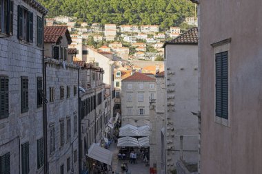 Dubrovnik 'in yoğun, tarihi kireçtaşı binalarının arasından geçen canlı bir sokak yılanı. Arka planda dağ evleri var..