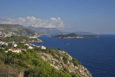 Dubrovniks kıyılarının panoramik manzarası, berrak mavi suları ve yemyeşil uçurumlarıyla, bulutlarla kaplı bir gökyüzünün altında