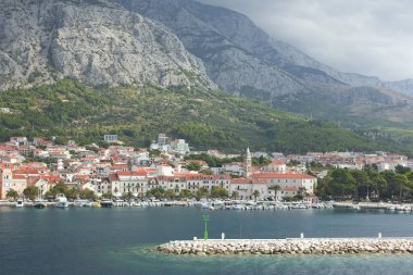 Dubrovniks kıyılarının panoramik manzarası, berrak mavi suları ve yemyeşil uçurumlarıyla, bulutlarla kaplı bir gökyüzünün altında