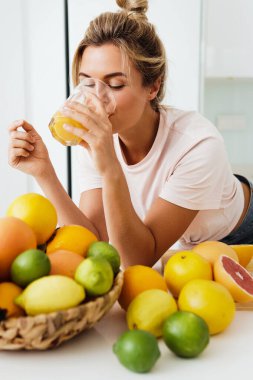 Beyaz mutfakta taze sıkılmış portakal suyu içen genç bir kadın.