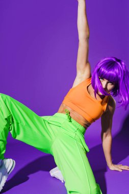 Dertsiz aktif kadın dansçı renkli spor giyerek mor arka plana karşı gösteri yapıyor.