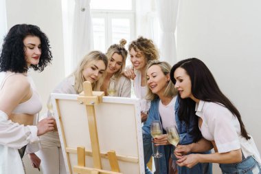 Bir grup güzel kadın tuvale resim yapıyor ve evde parti sırasında beyaz şarap içiyor.