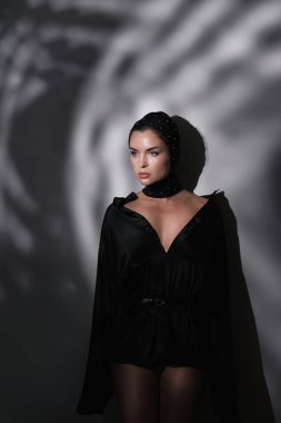 Gösterişli bir maske takan, yaratıcı stüdyo ışığıyla süslenmiş genç bir kadının moda portresi.