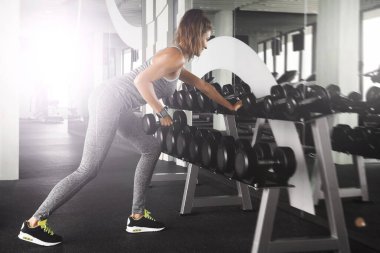 Genç ve güzel kadın spor salonunda dumbbells ile çalışma dışarı