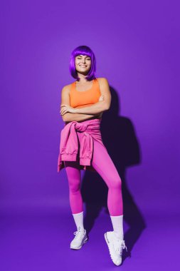 Renkli spor kıyafetleri giyen neşeli bir kadının portresi mor arka planda oturuyor.