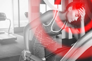 Modern spor salonunda spor yaparken acı veren baş ağrısı çeken genç bir kadın.