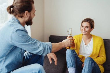 Genç, neşeli bir çift kanepede oturuyor ve evde bira içiyor.