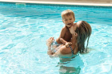 Mutlu anne ve küçük tatlı oğlu yaz tatilinde açık havuzda yüzüyorlar.