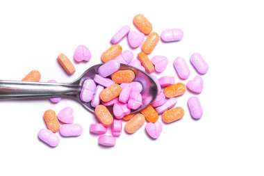 Metalik bir kaşık ve beyaz arka planda renkli hapların yakın plan çekimi..