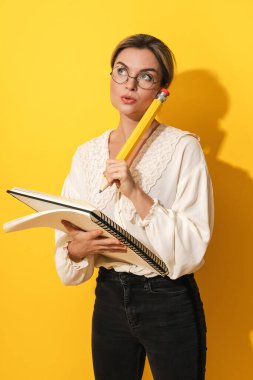 Sarı arka planda büyük bir kalem ve defter tutan düşünceli genç bir kadın.